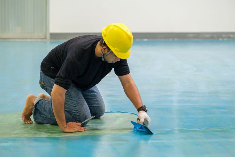 worker installing epoxy flooring on concrete floor