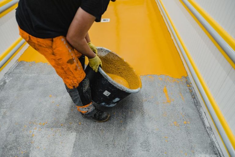 Worker adding sand-like anti-slip additive into wet yellow epoxy coating